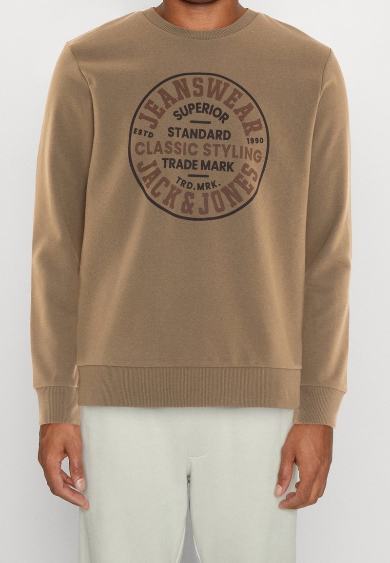 Sudadera marrón con un gran logo circular que dice "JEANSWEAR JACK & JONES." Puños y dobladillo acanalados, textura de tela suave.