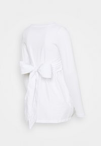 Vit långärmad topp med en rosettdetalj på baksidan. Slätt tyg, avslappnad passform, med rynkade sidor för formning.