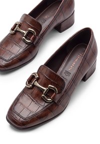 Chaussures basses en cuir marron avec texture crocodile et détail métallique mors de cheval sur le dessus, vues de dessus sur fond blanc.