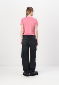 Camiseta rosa de manga corta, pantalones cargo negros con bolsillos laterales y zapatos de plataforma negros. Diseño simple, corte relajado, aspecto general casual.
