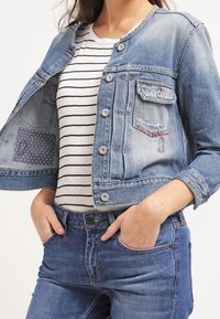 Ljusblå denimjacka med croppad längd, rund halsringning, framknäppning, en bröstficka och randig mönstring på innerfodret.