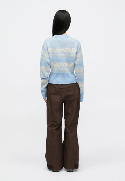 Ανοιχτό μπλε πλεκτό πουλόβερ με επαναλαμβανόμενο μοτίβο λογοτύπου, συνδυασμένο με καφέ παντελόνια cargo. Το πουλόβερ διαθέτει ριμπ τελείωμα και μανσέτες.