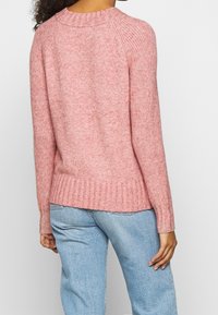 Pull en tricot rose pâle avec un ourlet et des poignets côtelés, doté d'un col arrondi et de manches raglan, présenté sur un fond neutre.
