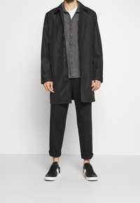 Black raincoat with a front zipper, gray button-up shirt beneath, black pants, and black sneakers with white accents. Smooth texture, casual design.