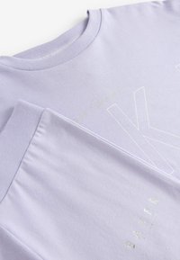 Lavendel bomull t-shirt med rund hals, korta ärmar och en mjuk textur. Har en vit grafisk design och subtila metalliska detaljer.