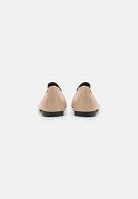 Chaussures slip-on en faux cuir nude avec un accent noir à l'arrière et une semelle basse noire. Texture lisse avec un minimum de détails.