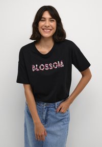 Čierne bavlnené tričko s krátkymi rukávmi, zdobené kvetinovou výšivkou, ktorá slovo "BLOSSOM" píše ružovou a bielou farbou na jednom farebnom pozadí.
