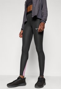 Sorte leggings med pink sidepanel, lavet af strækbart materiale. Sammen med en sort top og en let grå jakke samt sorte atletiske sko.