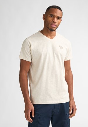 T-shirt beige à col en V, confectionné dans un tissu texturé et léger, avec des manches courtes et un petit logo sur le côté gauche de la poitrine.