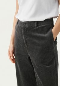 Pantalon en velours côtelé gris avec texture à côtes verticales, doté d'une taille traditionnelle, de poches latérales et d'une coupe décontractée.