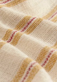 Tissu tissé en crème avec des rayures jaunes et rouges. La surface texturée présente un tissage lâche, renforçant l'apparence légère et aérée.