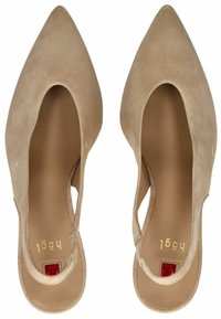 Tacones en beige de ante, con tirante al tobillo, puntera afilada, lados abiertos y un pequeño acento rojo en el tacón. Forro interior suave y diseño minimalista.