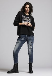 Black hooded sweatshirt with white graphic print; distressed blue jeans with multiple rips; black combat boots with textured finish.