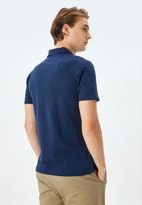 Marineblauw polo shirt met korte mouwen en een textuurafwerking, voorzien van een klassieke kraag en een rechte zoom, gedragen met khaki broek.