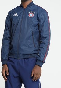 Navy blue Adidas bomber jacket with red accents and a Bayern Munich logo. Features a zip closure and ribbed cuffs.