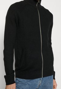 Svart ribbat zip-up-tröja med hög krage, har sidofickor och en texturerad yta. Mjuk tyg, figurnära design.