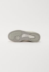 Weiße Sportschuhe mit einer strukturierten Gummisohle mit Zickzackmustern, Markenlogo und glattem, mattem Obermaterial.