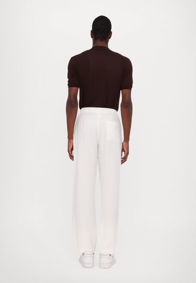 Brown short-sleeve top paired with white wide-leg pants featuring an elastic waistband and a back pocket, worn with white sneakers.