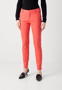 Koraalroze op maat gemaakte broek met een slanke pasvorm, een gladde textuur en een tailleband op heuphoogte, gecombineerd met glanzende zwarte pumps met puntige neus.