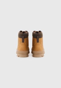 Botas de piel marrón hasta el tobillo con un cuello de punto marrón texturizado, suela de goma y tiradores, que destacan por un diseño robusto y resistente.