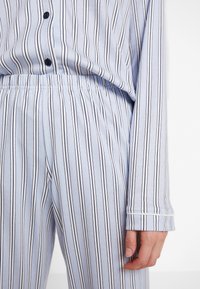 Ljusblå pyjamasset med vertikala svarta ränder, bestående av en knappad skjorta och byxor med elastisk nederdel och en slät textur.