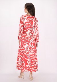 Rochie lungă, cu straturi, care prezintă un model abstract roșu și alb. Fabricată dintr-un material moale, cu mâneci lungi și talie ajustată.