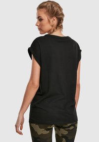 Mustast puuvillast T-särk rullitud varrukatega, lõdva lõike ja lihtsa tagaküljega. Sobitatud roheliste camo leggingutega.