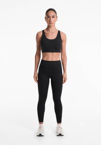 Îmbrăcăminte sport neagră formată dintr-un sutien sport ajustat și leggings cu talie înaltă, realizată dintr-un material elastic, cu o textură netedă și cusături minime.