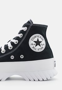 Baskets montantes en toile noire avec des lacets blancs et une semelle en caoutchouc. Elles présentent un patch rond avec un logo en étoile sur le côté et des détails en couture blanche.