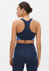 Sujeción deportiva de color azul marino con diseño de tirantes en la parte posterior, que presenta detalles en azul claro y un acabado texturizado en los laterales. Tejido suave.