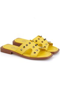Gelbe Leder-Sandalen mit flacher Sohle, offenes Zehendesign und dekorativen silbernen Nieten entlang der Riemen. Glatte Textur und leicht glänzend.