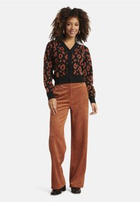 Black cardigan with brown leopard print, long sleeves, and button-front design, paired with high-waisted, wide-leg brown pants and black boots.