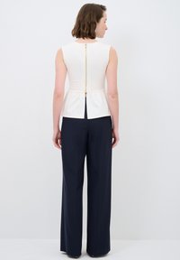 Ärmelloses cremefarbenes Top mit einem Reißverschluss auf der Rückseite, kombiniert mit hochgeschnittenen marineblauen Hosen. Glattes Material, taillierte Passform mit einem Peplum-Detail.