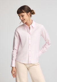 Ljusrosa knapp-up skjorta gjord av mjuk bomull, med en traditionell krage, långa ärmar och en lätt bågformad nederkant.