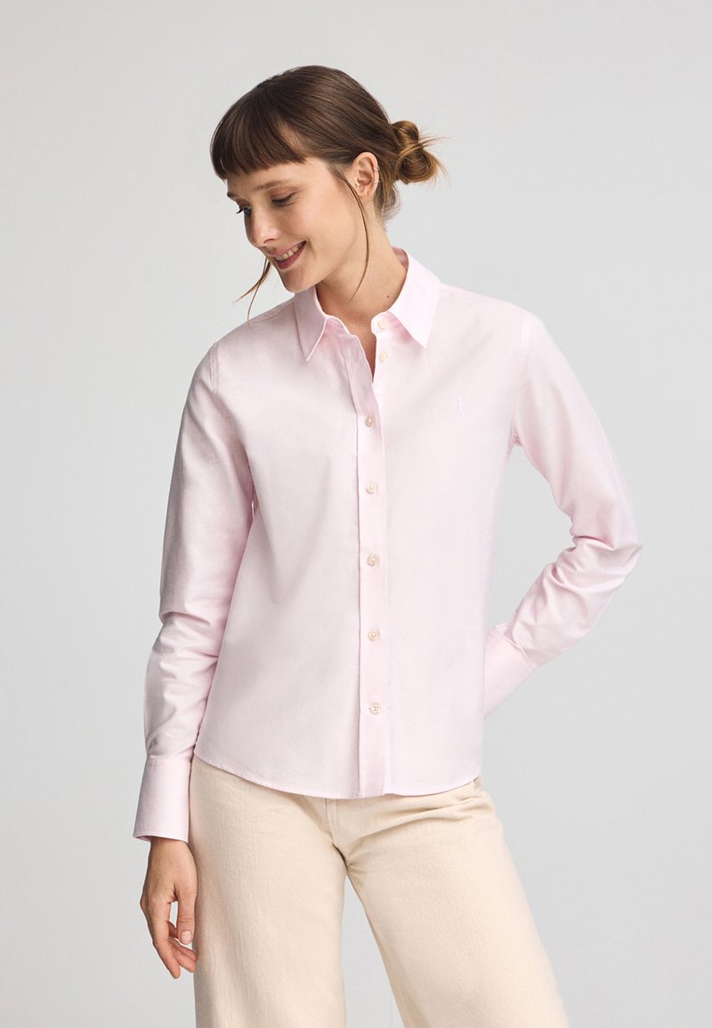 Ljusrosa knapp-up skjorta gjord av mjuk bomull, med en traditionell krage, långa ärmar och en lätt bågformad nederkant.