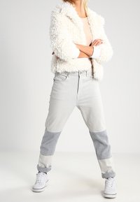 Puszysta biała kurtka, jasny top i dwutonowe dżinsy w kolorach szarym i kremowym. Białe trampki dopełniają strój.