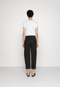 Witte t-shirt met korte mouwen en zwarte cropped broek, met een rechte snit en minimalistisch ontwerp, gecombineerd met platte zwarte sandalen.