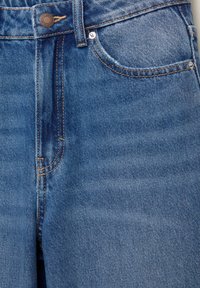 Közép kék színű farmernadrág magas derékkal, elöl gombos és cipzáras záródással, hagyományos zsebmintával és jól látható varrással.