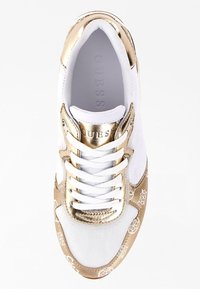 Baskets blanches avec accents dorés, dotées d'une tige en mesh, d'un bout rond et d'une fermeture à lacets. Logo notable sur la languette et motifs décoratifs.