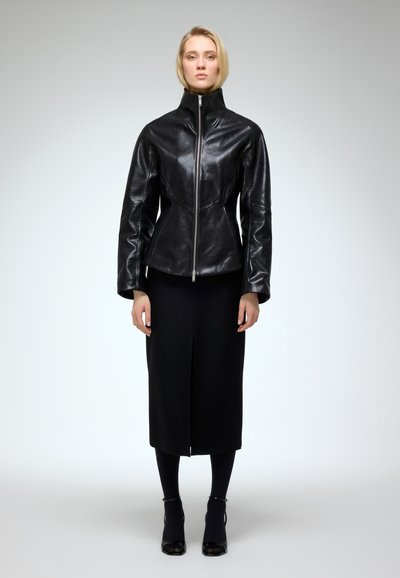 Black leather jacket with a high collar and front zipper, featuring a tailored fit and panel seams; paired with a black midi skirt and ankle boots.
