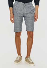 Szare szorty w kratę o dopasowanym kroju, z luźnym fasonem, z zapięciem na guzik i przednimi kieszeniami. Noszone z beżowymi zamszowymi sneakersami.