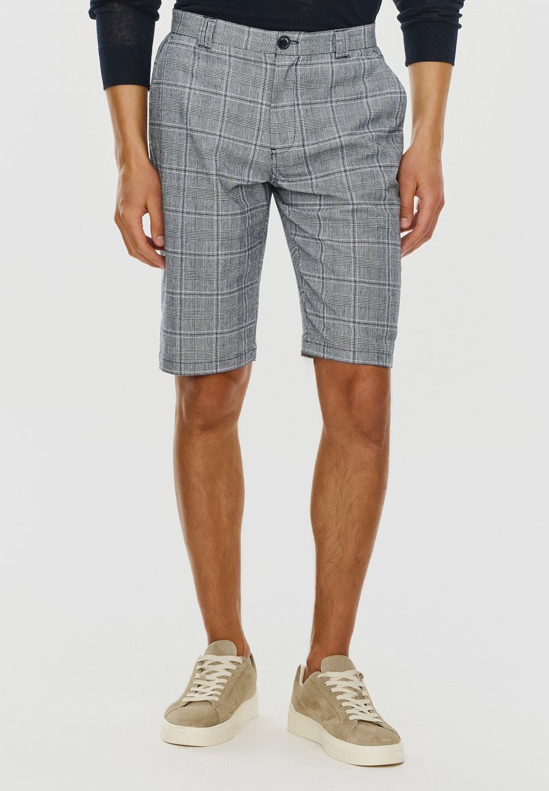 Szare szorty w kratę o dopasowanym kroju, z luźnym fasonem, z zapięciem na guzik i przednimi kieszeniami. Noszone z beżowymi zamszowymi sneakersami.