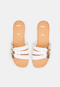 Sandales blanches à soufflet avec trois brides croisées, présentant un accent métallique doré. Semelle lisse avec une semelle intérieure beige affichant "Bata" et "Design Italien."
