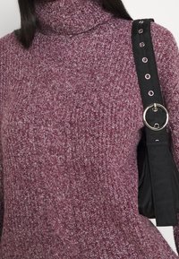 Knitted turtleneck sweater in a lavender hue, featuring a textured pattern. Black strap with silver hardware visible.