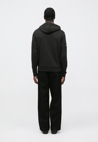 Μαύρο φούτερ με κουκούλα και κορδόνι, ριμπ τελείωμα και μακριά μανίκια. Συνδυάζεται με αντίστοιχο φαρδύ μαύρο παντελόνι, και τα δύο από λείο ύφασμα.