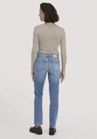 Vaaleanbeige pitkähihaisen paidan parina ovat vaaleansiniset suorat farkut. Farkuissa on takana ruskea nahkaleima ja ne ovat hieman haalistuneet.