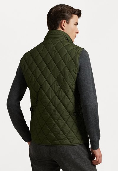 Izšūta olīvu zaļa veste ar augstu apkakli, pogu akcentiem un elegantu piegriezumu. Valkāta virs pelēka garām piedurknēm krekliņa, uz kura redzami dimanta raksti.