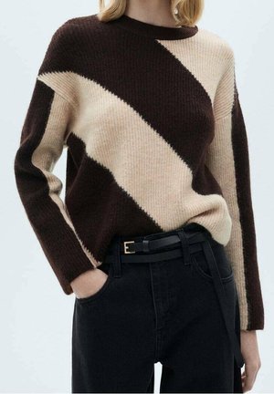 Person wearing a brown and beige diagonal color-block sweater with long sleeves tucked into high-waisted black pants with a black belt.