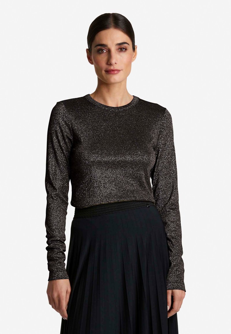 Schwarzes Langarmshirt mit texturierter, glitzernder Oberfläche und rundem Ausschnitt, kombiniert mit einem plissierten schwarzen Rock.
