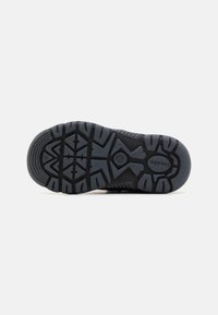Suola di scarpa in gomma nera con un motivo di presa testurizzato e un design del battistrada prominente, con un logo in rilievo e accenti esagonali.
